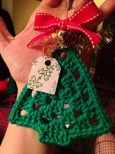 a hand holding a green crocheted christmas tree ornament with a red bow