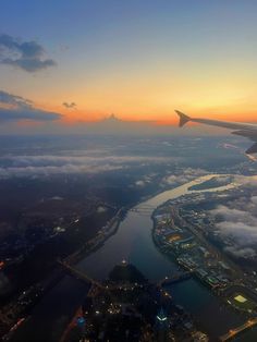 an airplane wing flying over the city lights and water at sunset or dawn with clouds