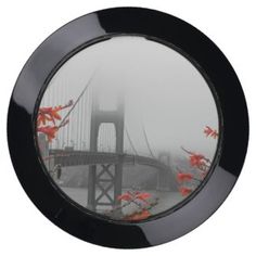 a mirror with the reflection of a bridge and flowers in front of it on a foggy day