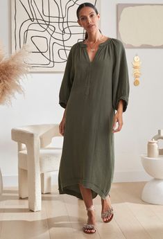 Woman walking wearing ocean+main Green Gauze Dress with Pockets Limited Edition Daywear Relaxed Fit Tunic With Split Neck, Relaxed Fit Split Neck Tunic For Daywear, Fall Vacation Tunic With Relaxed Fit, Fall Vacation Cotton Tunic, Bohemian Tunic For Daywear With Relaxed Fit, Bohemian Tunic With Relaxed Fit For Daywear, Casual Long Sleeve Kaftan For Loungewear, Cotton Maxi Dress With Relaxed Fit, Unlined, Chic Long-sleeved Kaftan With Relaxed Fit