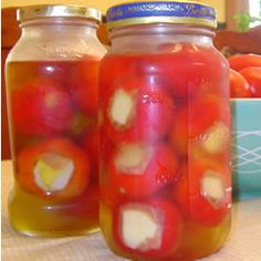 two jars filled with pickled tomatoes on top of a table next to oranges