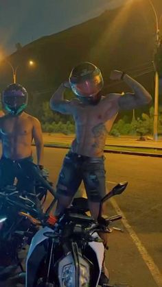 two shirtless men standing next to motorcycles on the street at night with their backs turned