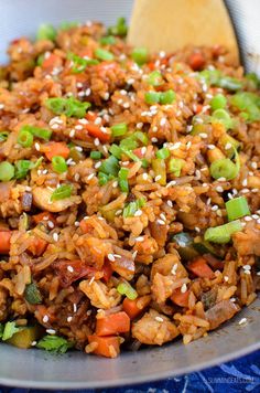 a bowl filled with rice and vegetables on top of a blue cloth next to a wooden spoon