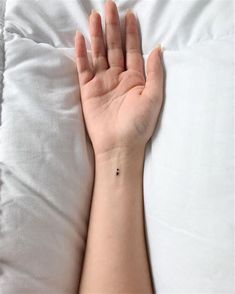 a person's hand with a small tattoo on it, resting on a pillow