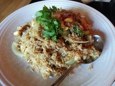 a white plate topped with rice covered in sauce and garnished with cilantro