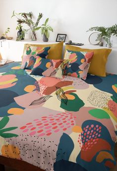 a bed with colorful sheets and pillows on top of it next to potted plants