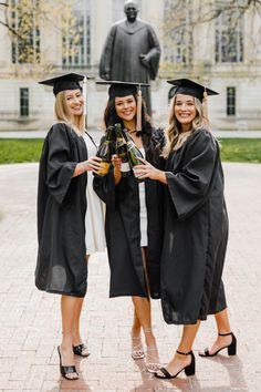 three women in graduation gowns posing for the camera with a statue in the background