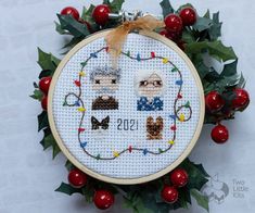 a cross stitch christmas ornament hanging from a hoop with holly and red berries