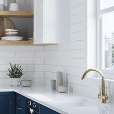 a kitchen with blue cabinets and white counter tops, gold faucet, and open shelving