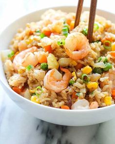 a bowl filled with shrimp and rice on top of a marble counter topped with chopsticks