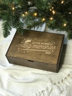 a wooden box sitting on top of a blanket next to a christmas tree with lights