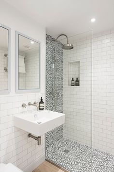 a white bathroom with black and white tile on the floor, shower stall and sink