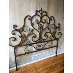 a metal headboard with ornate scroll work on the top and bottom, against a wall