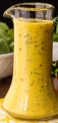 a glass pitcher filled with yellow liquid sitting on top of a table next to vegetables