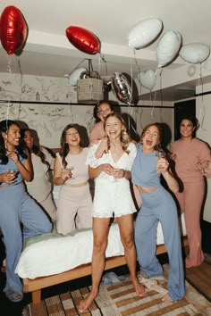 a group of women standing next to each other in front of a bed with balloons hanging from the ceiling