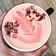 a hand holding a cup filled with pink liquid and dried flowers on the rim, in front of a tiled floor