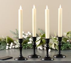 four candles are sitting on a table next to some flowers and a cell phone in front of them