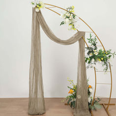 an arch decorated with flowers and greenery on a wooden floor in front of a white wall