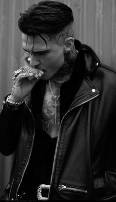 a man with tattoos on his face eating a piece of pizza while wearing a leather jacket