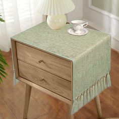 a table with a lamp on top of it next to a wooden drawer and plant