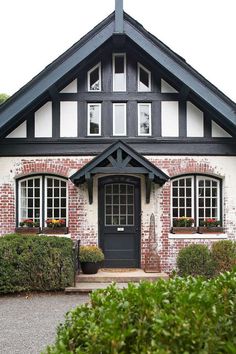 a black and white house with hedges around it's front door, surrounded by bushes