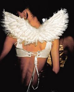 the back of a woman with white feathers on her neck and chest, wearing a bra