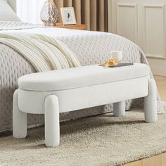 a white bench sitting on top of a bed next to a nightstand with a cup