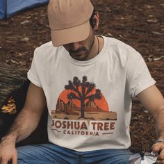 a man wearing a joshua tree california t - shirt sitting on a log in the woods