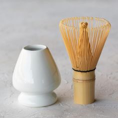 a white vase next to a bamboo whisk