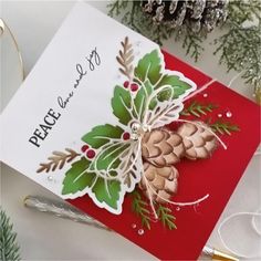 a christmas card with holly leaves and pine cones on it, sitting next to other holiday decorations