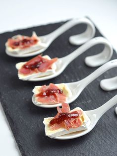 four spoons with food on them are sitting on a black tray and one is holding some sort of utensils