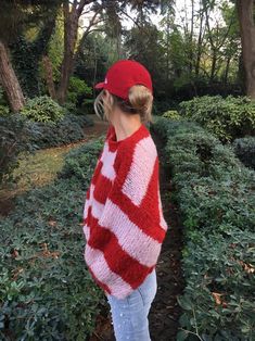 a woman wearing a red and white knitted sweater standing on a path in the woods