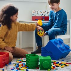 two children playing with legos on the floor in a playroom, one holding a yellow toy