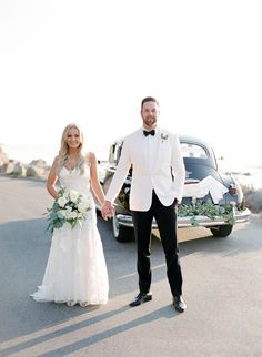 a bride and groom are holding hands in front of an old car on the road