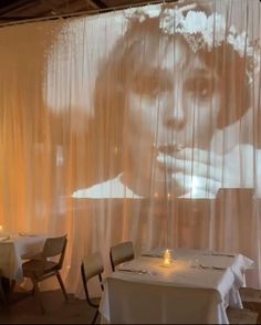 an image of a woman is projected on the wall behind two tables with white linens