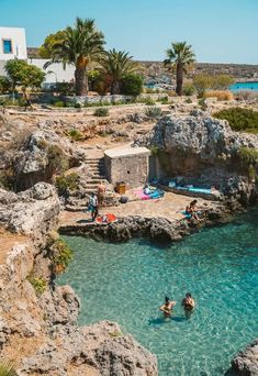 people are swimming in the blue water near some rocks and palm trees on the beach