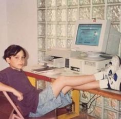 a young boy sitting at a desk in front of an old computer monitor and keyboard