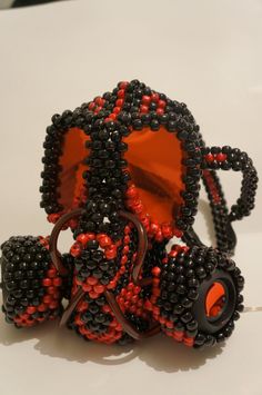 an orange and black beaded object sitting on top of a white table next to a pair of glasses