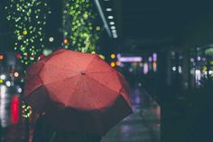 a person holding an umbrella on a rainy night in the rain with lights behind them