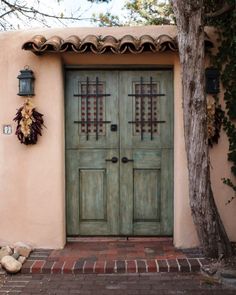 a green door with decorative iron work on the top and side panels, in front of a pink stucco building