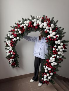 a woman standing in front of a christmas wreath with red and white balls on it