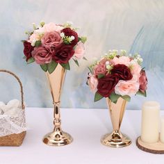 three gold vases with flowers in them on a table next to a basket and candle