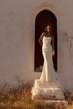 a woman standing in front of a doorway wearing a white dress and posing for the camera