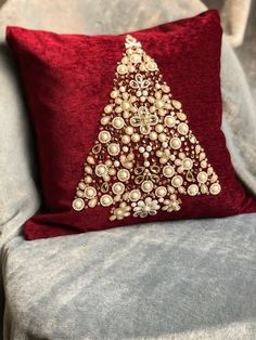 a red pillow sitting on top of a gray couch next to a white and gold christmas tree