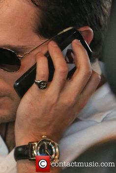 a man in sunglasses talking on a cell phone while holding his hand to his ear