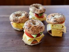 bagel sandwiches with cheese, tomato, and lettuce are arranged on a wooden table