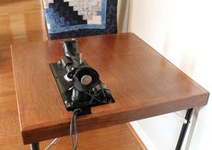 a camera sitting on top of a wooden table next to a quilted wall hanging