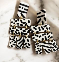 four black and white earrings on a marble counter top with gold hardware, one in the shape of zebra print