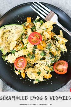 scrambled eggs and veggies on a black plate with a fork