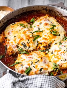 a pan filled with chicken parmesan covered in cheese and sauce on top of a wooden table